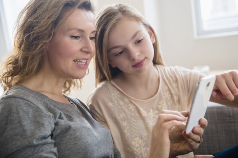 Caucasian mother and daughter using cell phone in living room