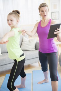 Caucasian mother and daughter practicing yoga with digital tablet