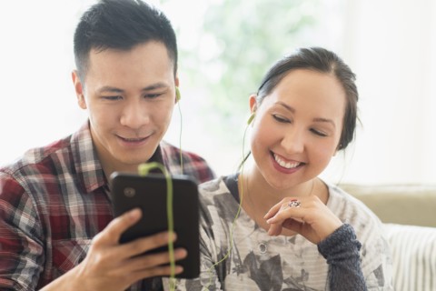 Laughing couple watching digital tablet on sofa