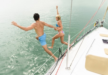Couple jumping from sailboat deck into ocean