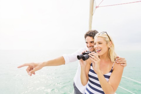 Couple looking out from boat deck with binoculars