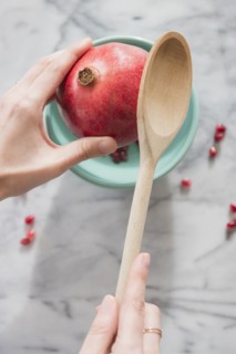 Close up of hands cracking pomegranate with spoon