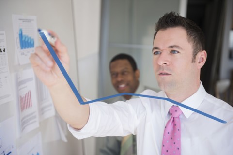 Businessman writing graph on glass wall in office