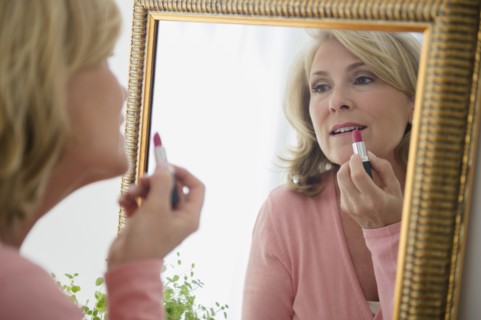 Caucasian woman applying lipstick in mirror