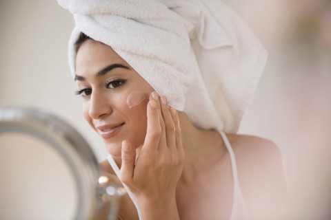 Woman with hair in towel rubbing lotion on face