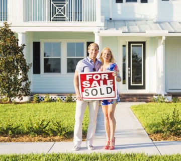 Caucasian couple holding sold sign outside new home