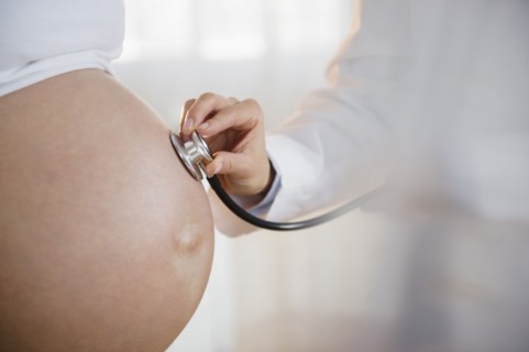 Doctor listening to belly of pregnant woman with stethoscope