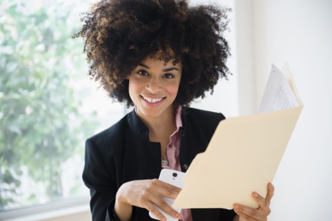 Mixed race businesswoman using cell phone near window