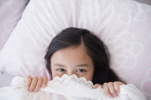 Girl peeking out from bed blankets