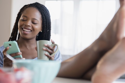 Black woman using cell phone and drinking coffee