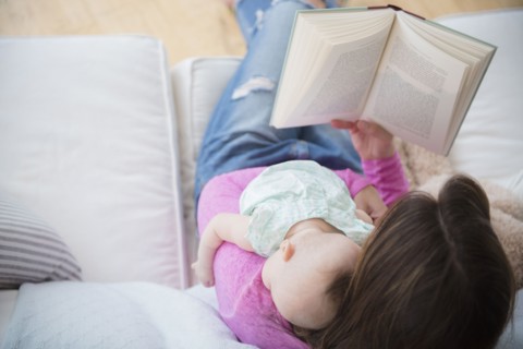 Mother reading book and holding baby daughter