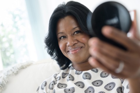 Black woman admiring herself in compact mirror