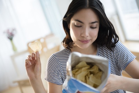 Hispanic woman reading ingredients on bag of potato chips