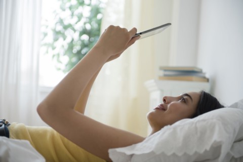 Hispanic woman using digital tablet in bed