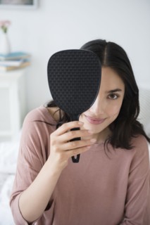 Hispanic woman peeking out from behind hand mirror