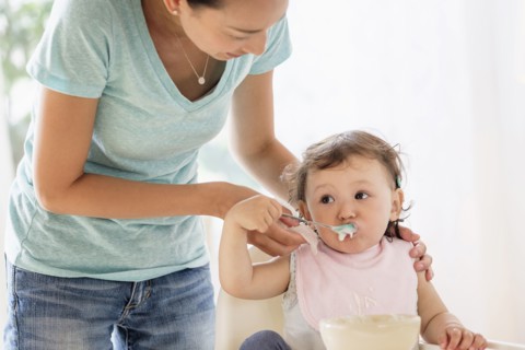 Mother feeding baby daughter in high chair