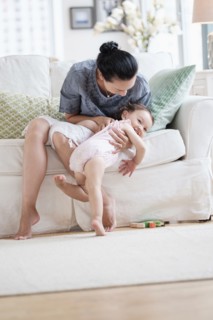 Mother playing with baby daughter on sofa
