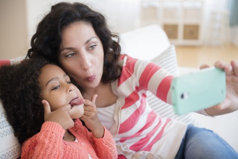 Mother and daughter taking selfie on sofa
