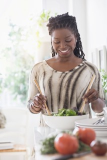 Black woman tossing salad in kitchen