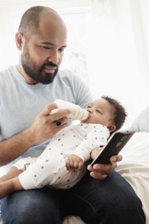 Father bottle feeding baby son and using cell phone