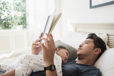Father reading with sleeping baby son