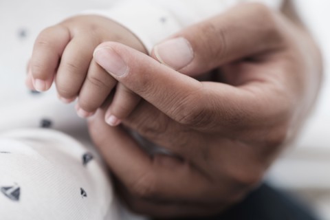 Close up of father holding hand of baby son