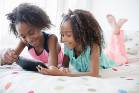 Mixed race sisters using digital tablet on bed