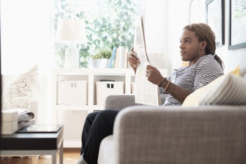 Mixed race man reading newspaper on sofa