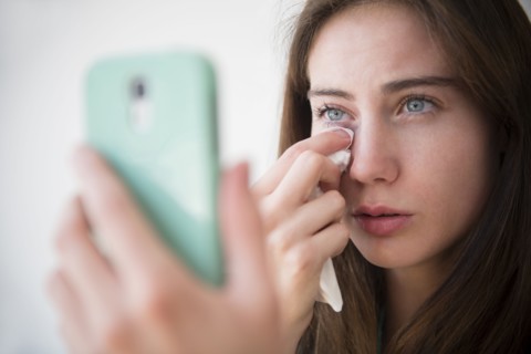 Native American woman with cell phone wiping away tears