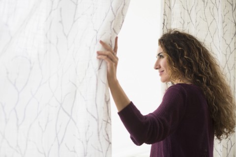 Mixed race woman looking out window curtain