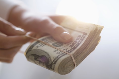 Hispanic woman holding rubber band around wad of cash