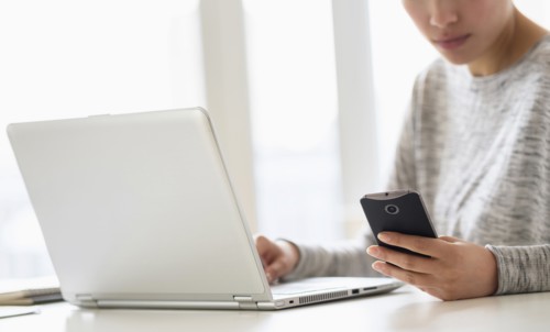 Hispanic woman using cell phone and laptop