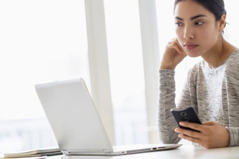 Hispanic woman using cell phone and laptop