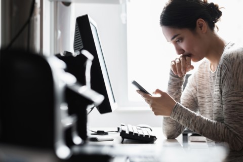 Hispanic woman using cell phone at computer