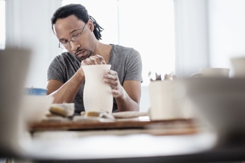 Black artist shaping ceramic vase in studio