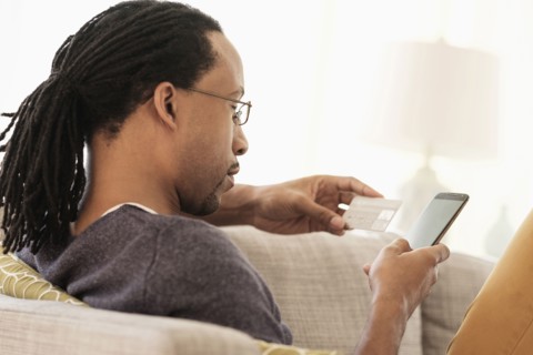 Black man shopping with cell phone on sofa