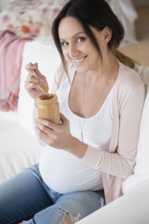 Pregnant Caucasian woman eating peanut butter from jar