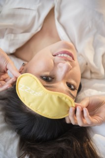 Smiling woman wearing eye mask on bed