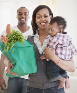 African couple holding baby and groceries in reusable bag