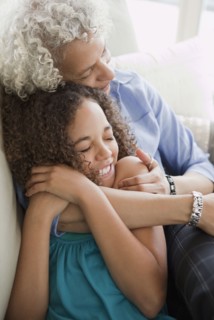 Grandmother and granddaughter hugging on sofa