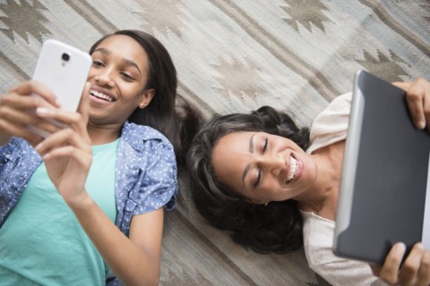 Mother and daughter laying on carpet using cell phone and digital tablet