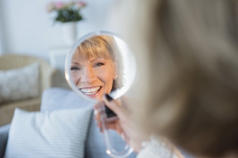 Older Caucasian woman smiling in handheld mirror