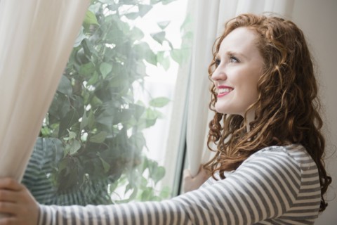 Caucasian woman opening curtains at window