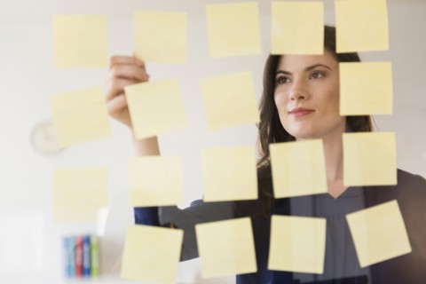 Caucasian businesswoman arranging adhesive notes on glass wall