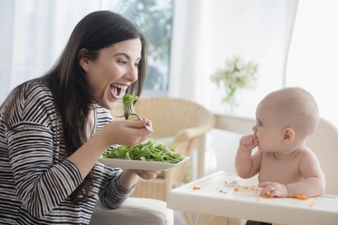 Caucasian woman eating salad while watching baby daughter