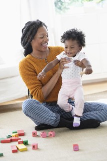 Black mother and baby daughter playing with blocks on carpet