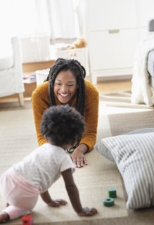 Black woman playing with baby daughter on carpet