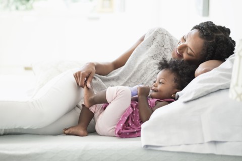 Black woman playing with foot of baby daughter on bed