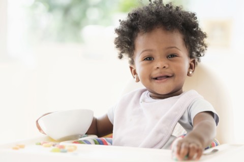 Smiling Black baby girl eating cereal from bowl in high chair