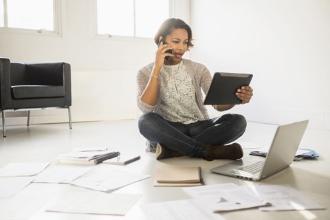 Black businesswoman using cell phone and digital tablet on floor